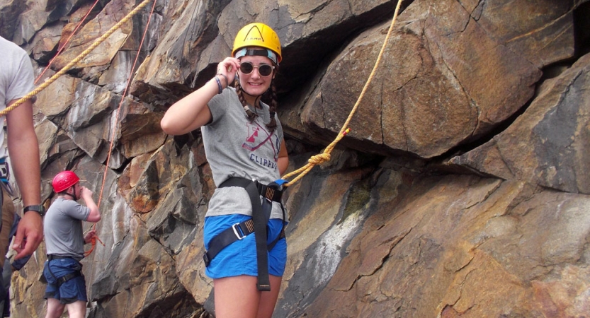 A person wearing safety gear is attached to a rope at the base of a rock wall. 